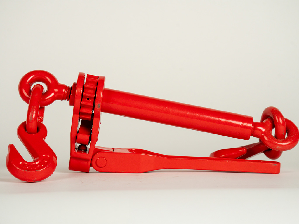 Heavy-duty ratchet load binder tightening a transport chain on a flatbed trailer, designed to securely fasten and stabilize heavy equipment during hauling.