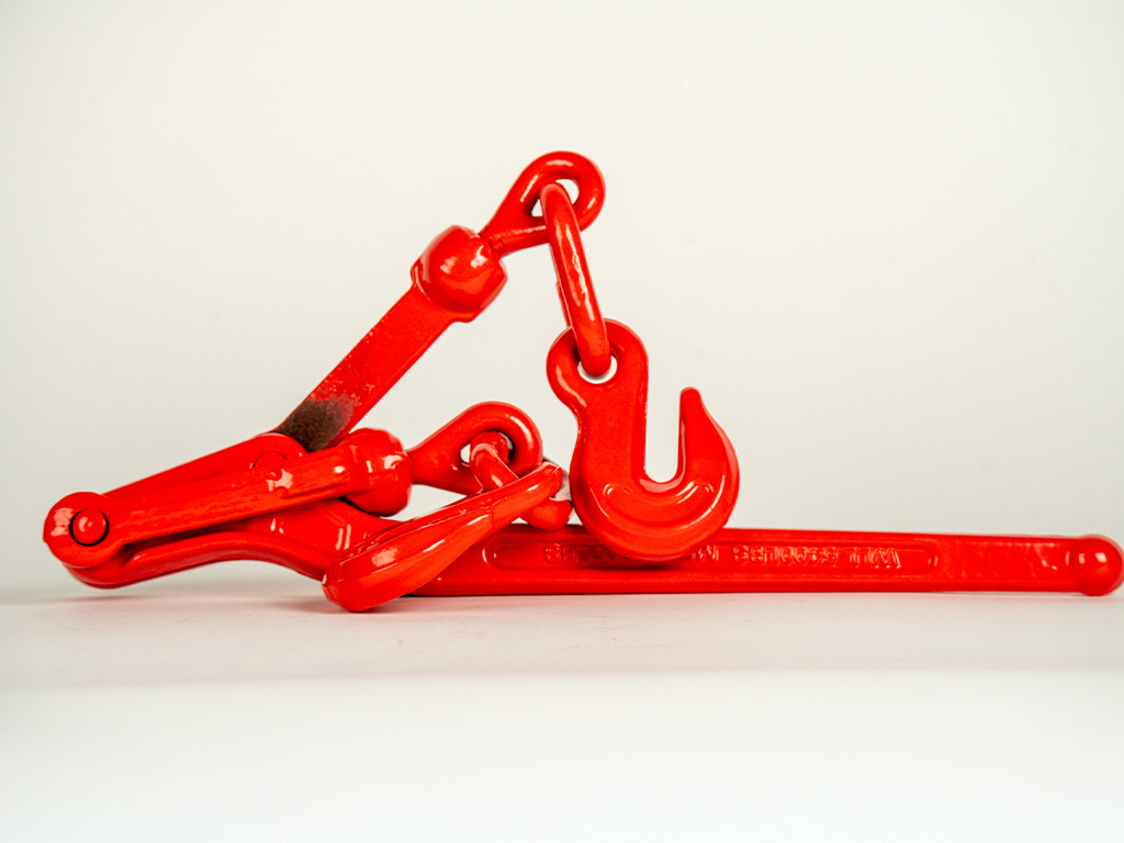 Lever-style load binder used to tighten and secure transport chains on a flatbed trailer, ensuring heavy equipment stays safely in place during hauling.