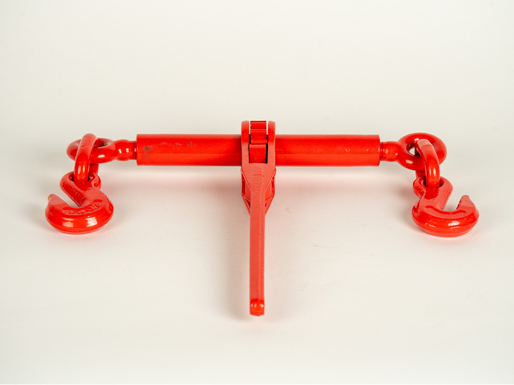 Ratchet load binder tightening a chain on a flatbed trailer, used for securing heavy equipment or cargo during transport.