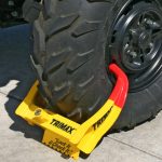 Trimax wheel chock lock secured around a trailer wheel, designed to prevent theft and unauthorized movement with heavy-duty steel construction and a bright visible finish.