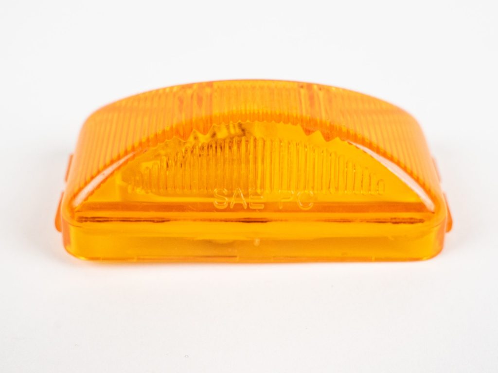 Amber plastic vehicle marker light cover stamped with "SAE PC" against a white background