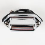 Front-angled view of a surface-mount chrome-hooded license plate light featuring a high-polish finish, two Phillips mounting screws, black foam mounting gasket, and wiring leads against a white background.